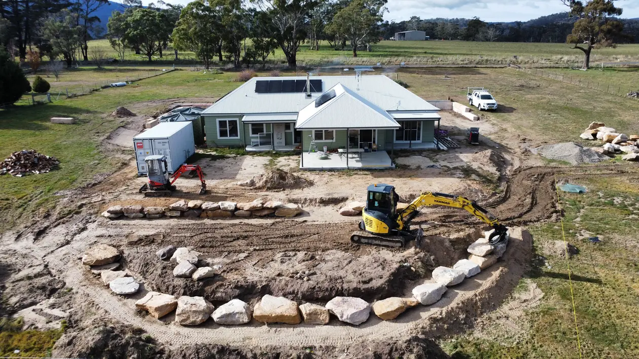 Excavator placing sandstone boulders for a curved retaining wall behind a house at Duckmaloi