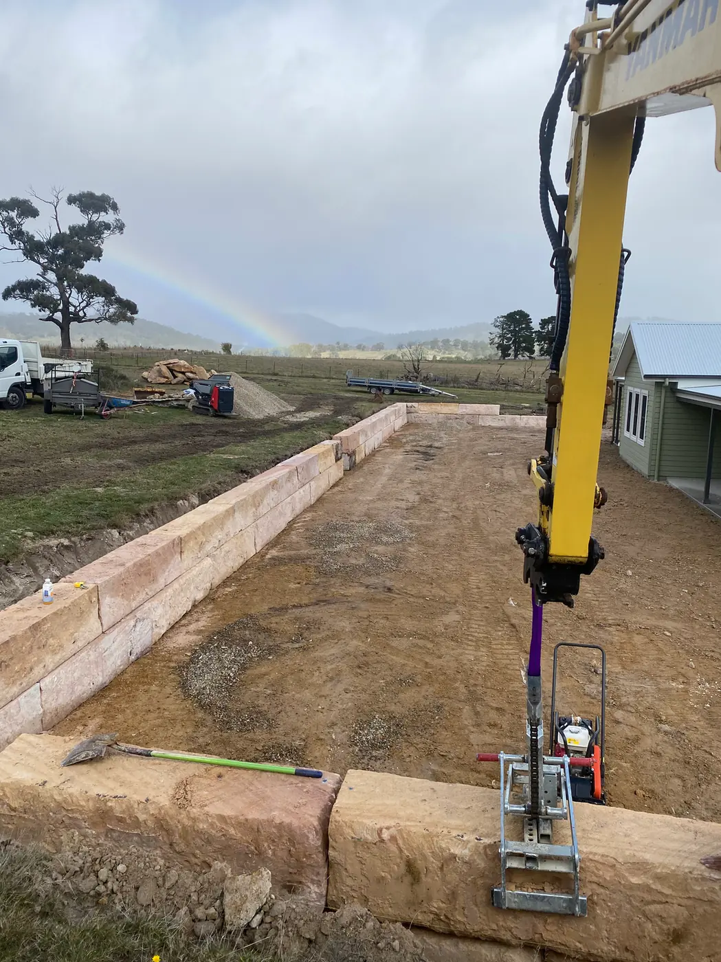 Excavator compacting fill behind a sandstone log retaining wall at Duckmaloi